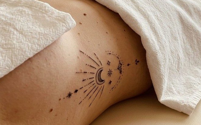 Tatuaje de una luna con rayos y estrellas en la piel